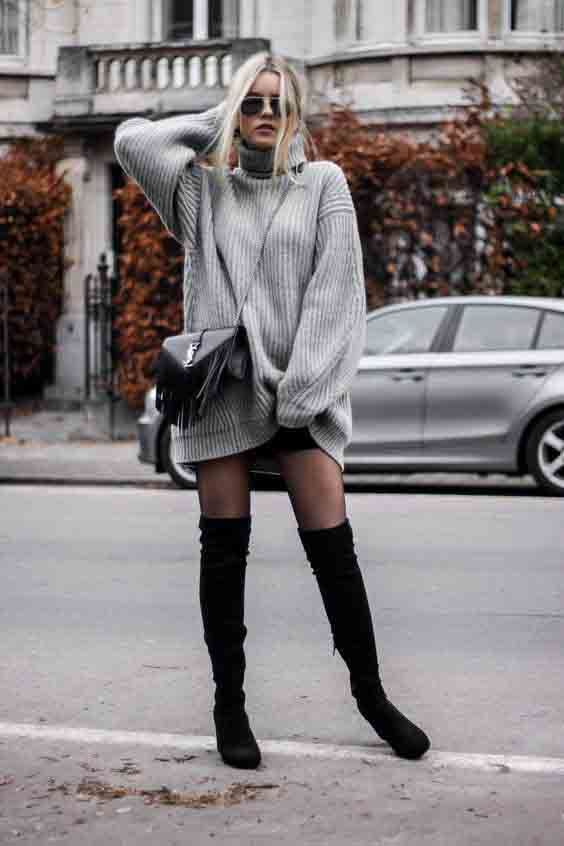 Mulher loira usando vestido suéter cinza oversized com botas pretas acima do joelho em rua urbana