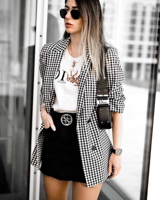 Mulher usando casaco xadrez preto e branco, camiseta branca e saia preta em ambiente urbano