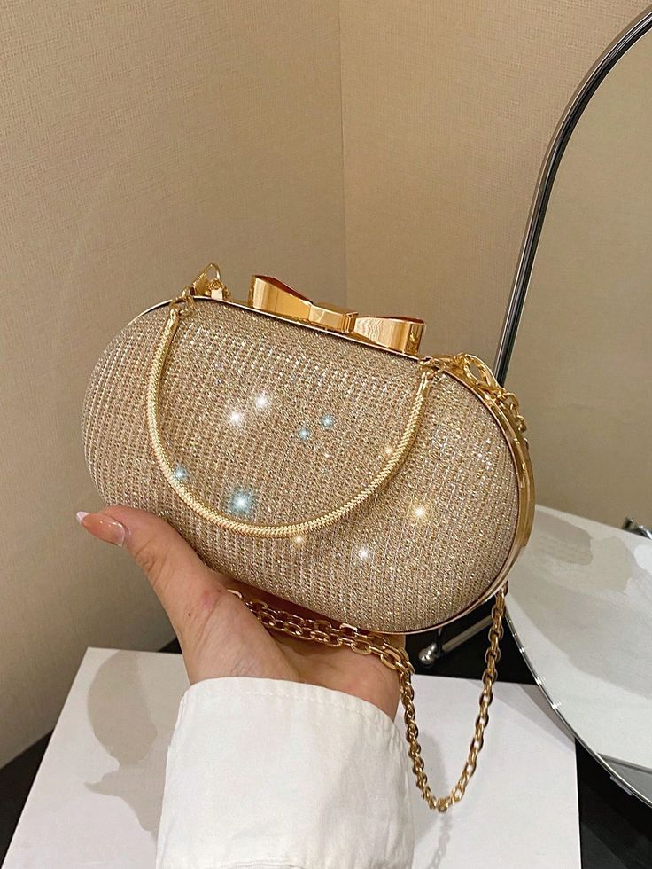 Bolsa de mão pequena dourada com detalhes brilhantes, corrente e fecho em forma de laço