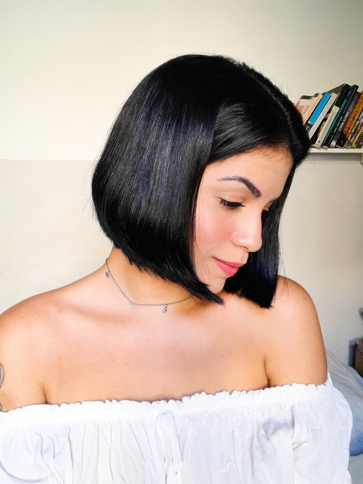 Mulher com cabelo preto estilo chanel curto, olhando para baixo, em ambiente interno.