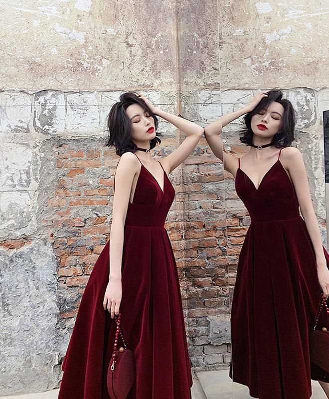 Mulher com vestido vermelho vinho longo, alças finas, segurando bolsa combinando, em frente a paredes de tijolos