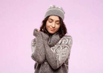 Mulher sorridente usando suéter cinza com estampa branca e gorro combinando, posando com os braços cruzados