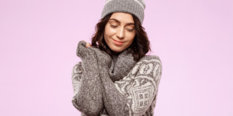 Mulher sorridente usando suéter cinza com estampa branca e gorro combinando, posando com os braços cruzados