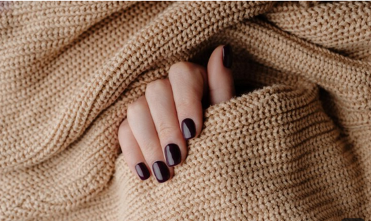 Mão feminina com unhas pintadas em tom preto clássico, segurando tecido de tricô bege.