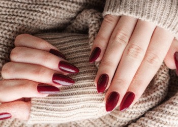 Mãos femininas com unhas marsala apoiadas em suéter bege de lã.