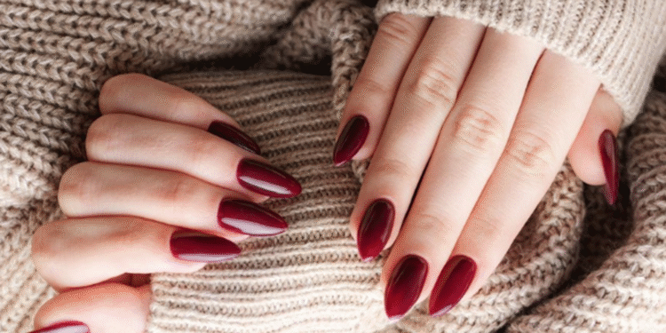 Mãos femininas com unhas marsala apoiadas em suéter bege de lã.