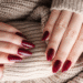 Mãos femininas com unhas marsala apoiadas em suéter bege de lã.
