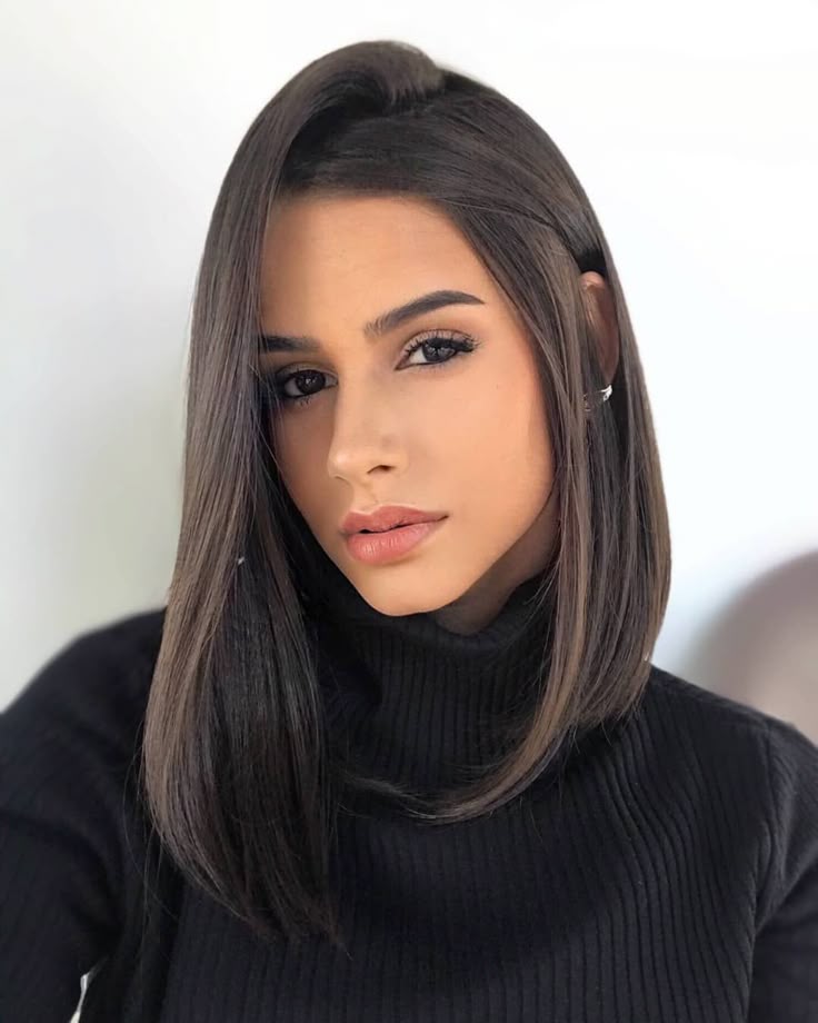Mulher com corte long bob, cabelo liso e escuro, usando suéter preto, olhando para a câmera.
