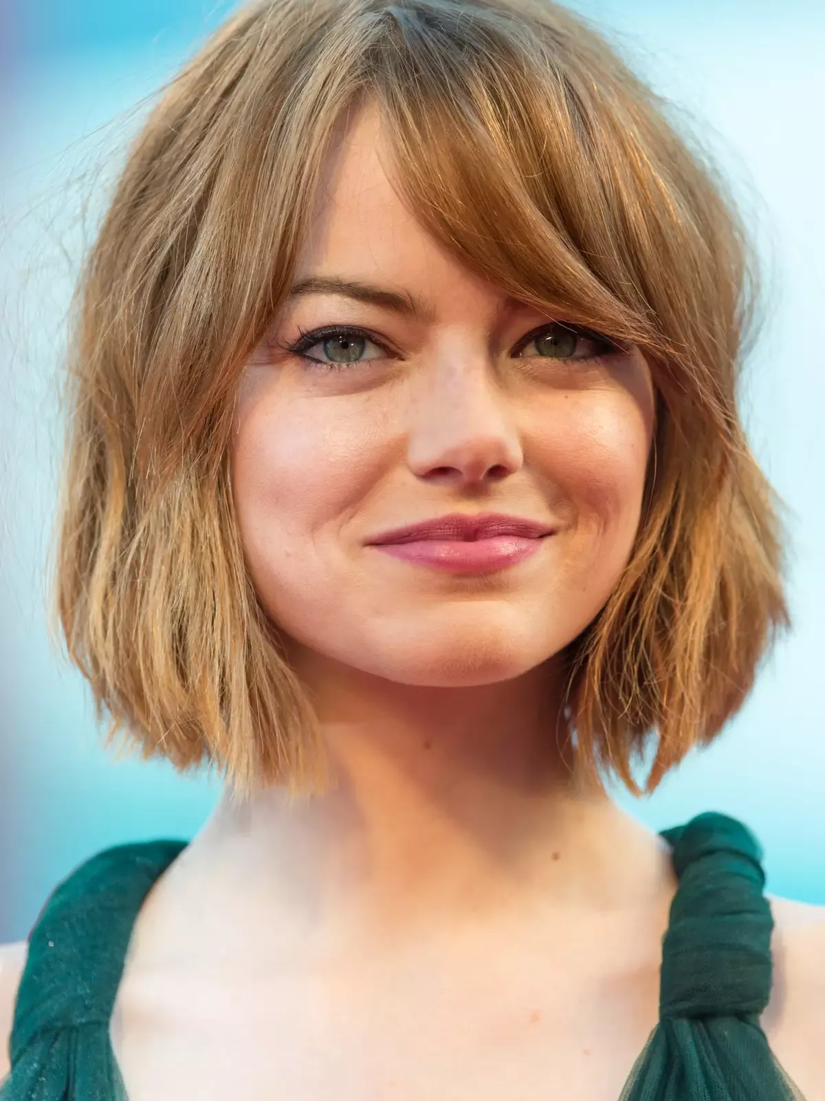 Mulher com corte de cabelo bob assimétrico em tom loiro, com pontas levemente desfiadas.