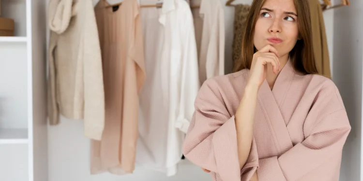 Como montar um guarda-roupa básico e versátil que facilita sua vida 1 Mulher pensativa escolhendo roupas neutras em um guarda-roupa minimalista