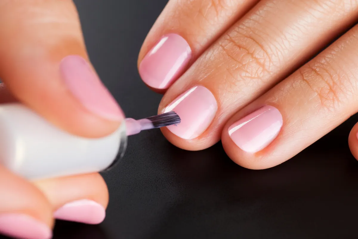Unhas sendo pintadas com esmalte rosa claro em fundo preto.