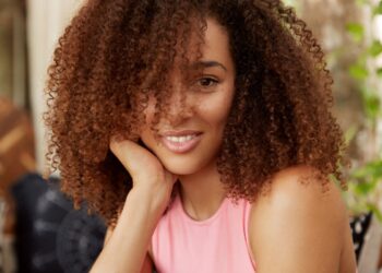 Mulher com cabelos cacheados castanhos em ambiente descontraído cuidando dos fios.