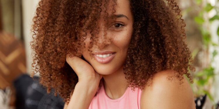 Mulher com cabelos cacheados castanhos em ambiente descontraído cuidando dos fios.