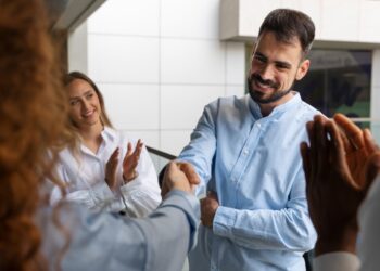 Homem apertando a mão de outra pessoa com colegas ao fundo