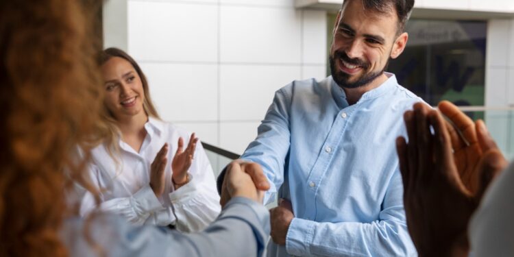 Homem apertando a mão de outra pessoa com colegas ao fundo