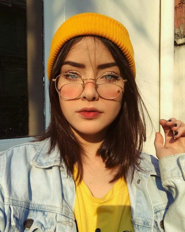 Mulher jovem usando gorro amarelo, óculos e jaqueta jeans em luz natural