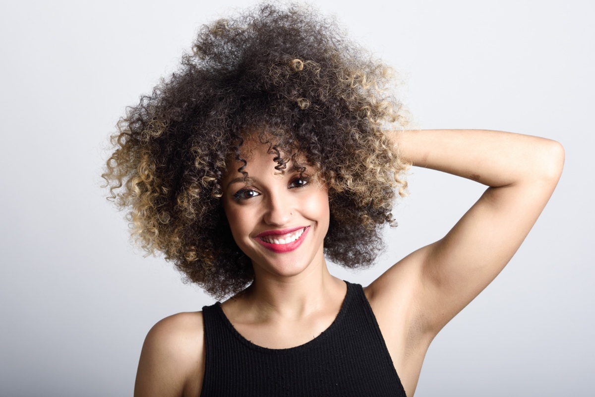 Mulher feliz com cabelos cacheados loiros destacando sua beleza natural.