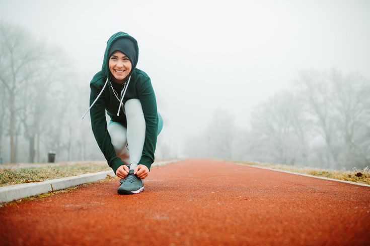 Mulher se preparando para correr em manhã fria de inverno com roupa de treino e capuz.