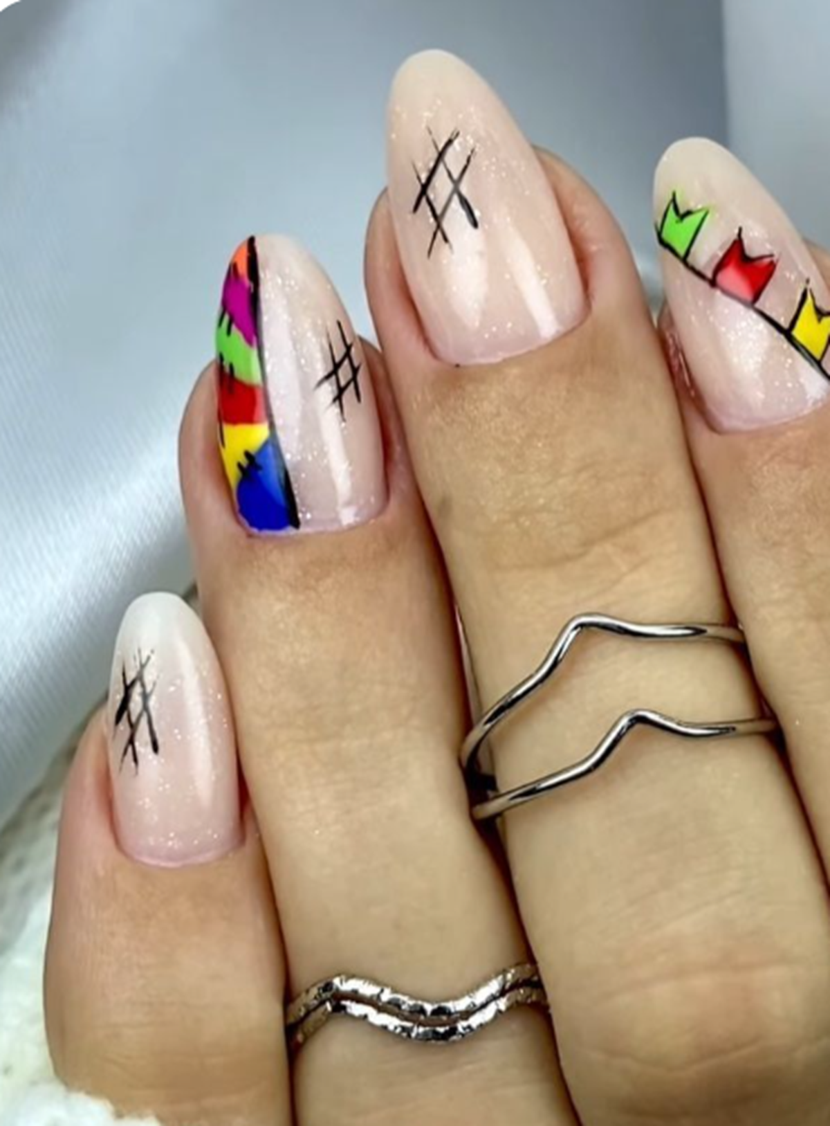 Unhas decoradas com desenhos de retalhos coloridos e linhas pretas, simulando patches.