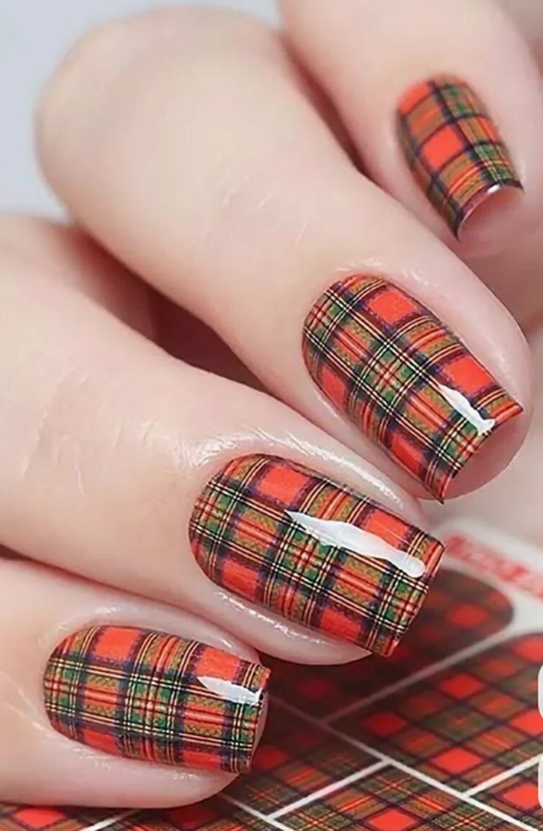 Unhas decoradas com estampa xadrez vermelha e preta combinadas com esmalte vermelho brilhante.