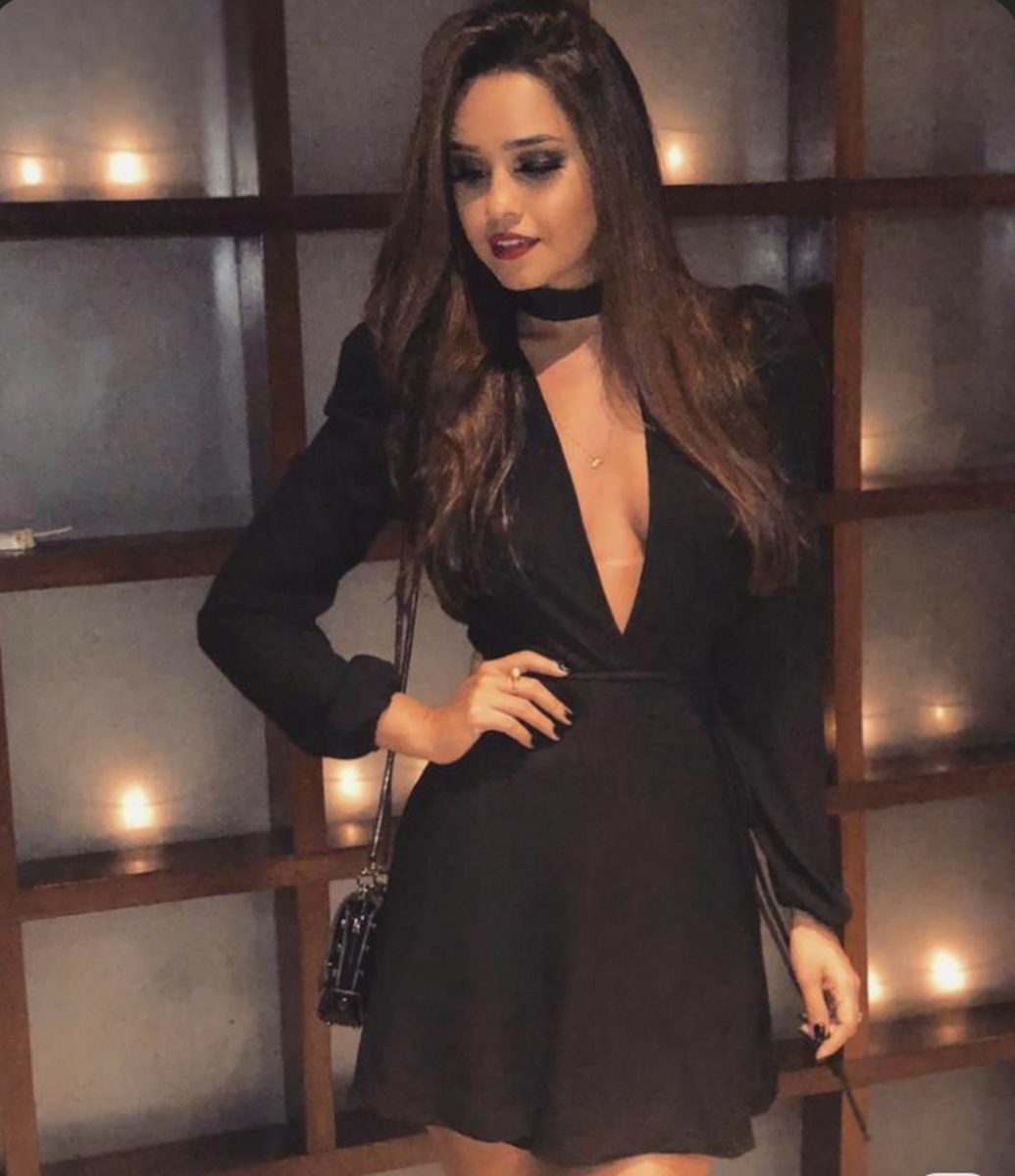 Mulher usando vestido preto de manga longa e decote profundo em ambiente noturno.