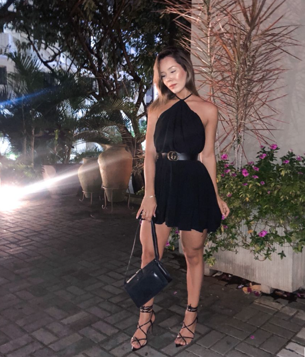 Mulher com vestido preto curto e sandália de salto em look sofisticado.
