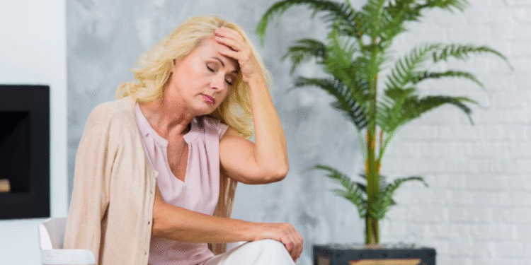 Mulher com expressão de desconforto e mão na cabeça, representando os sintomas das ondas de calor durante a menopausa.