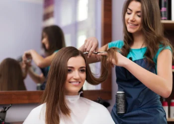 Profissional cortando cabelo de mulher com rosto oval em salão de beleza.