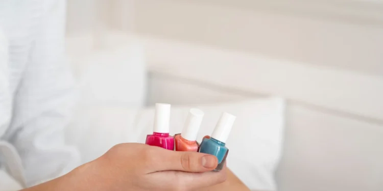 Três frascos de esmalte colorido em uma mão, representando a diversidade de opções para unhas. Ideal para escolher o esmalte perfeito para cada momento.