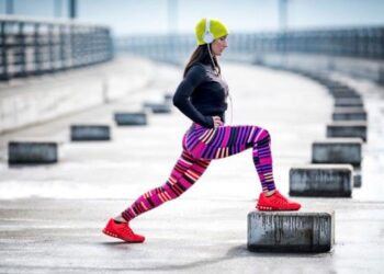 Mulher praticando exercício físico ao ar livre durante o inverno com roupas coloridas e touca.