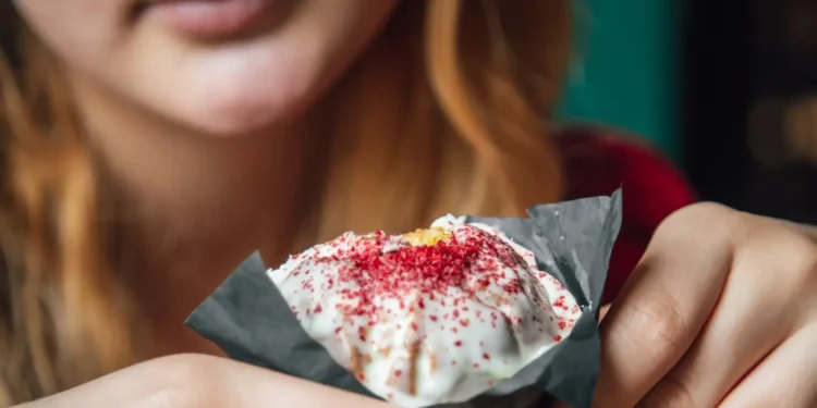 Jovem segurando um doce embrulhado em papel preto com cobertura branca e confeitos vermelhos