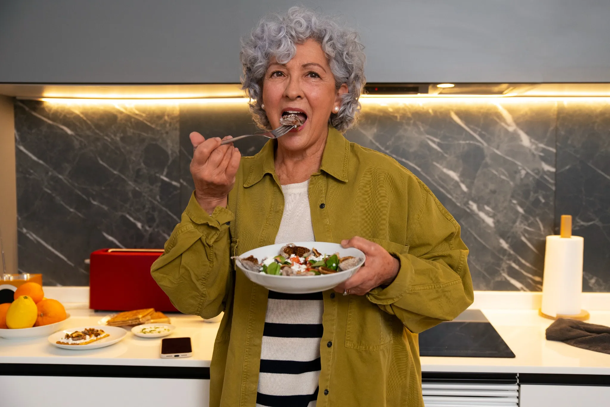 Mulher idosa comendo uma refeição saudável, destacando a importância da alimentação para a saúde da pele e cabelo.