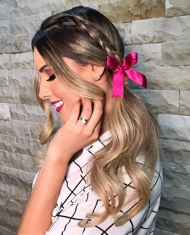 Mulher com cabelo preso em trança lateral e laço rosa decorativo.