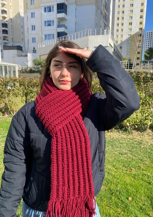 Mulher ao ar livre usando um cachecol volumoso vermelho cereja com jaqueta preta e ambiente ensolarado.