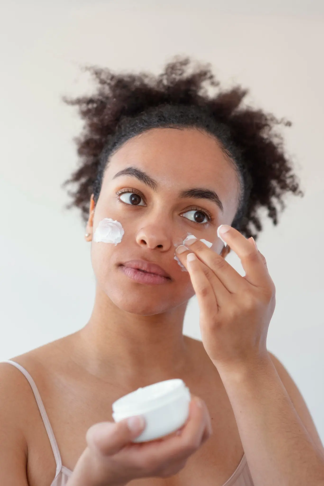 Mulher aplicando creme hidratante no rosto para cuidar da pele.