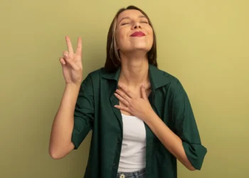 Mulher feliz com gesto de vitória, demonstrando autoconfiança, com a mão no peito e sorrindo