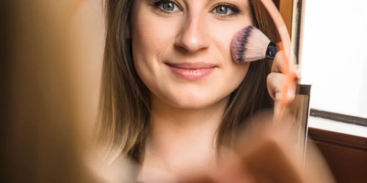 Mulher sorridente aplicando maquiagem leve e natural com blush no rosto.