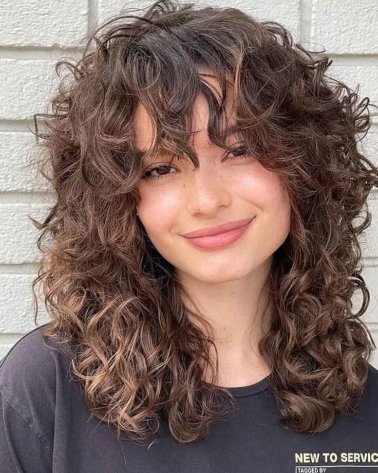 Mulher com cabelo cacheado cortado em estilo borboleta, destacando camadas e movimento