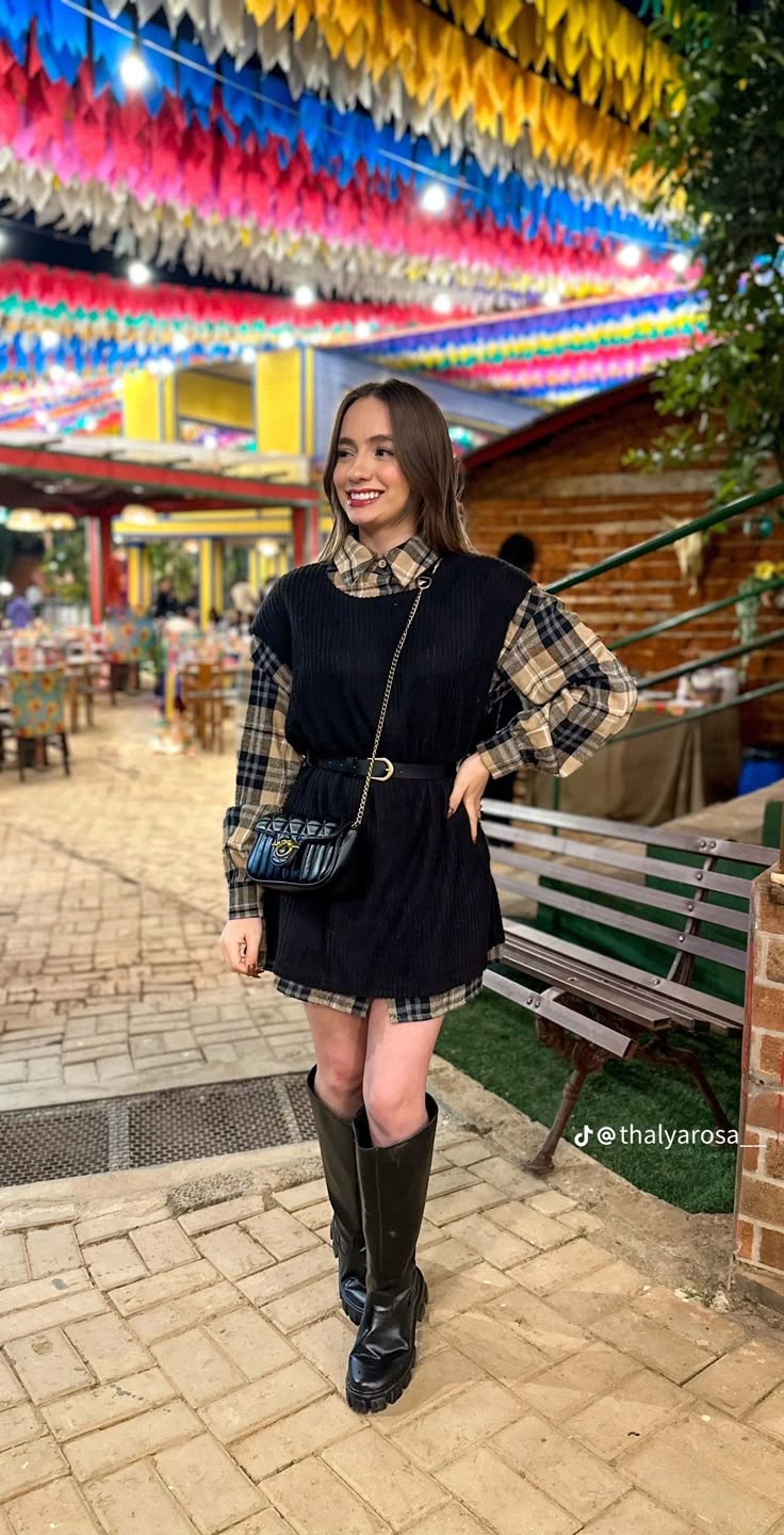 Mulher em festa junina com look moderno usando camisa xadrez e vestido preto sobreposto com bota cano alto