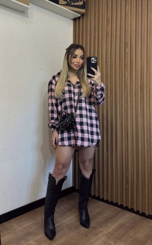 Mulher usando camisa xadrez oversized em rosa e preto com bota western preta, em look para festa junina