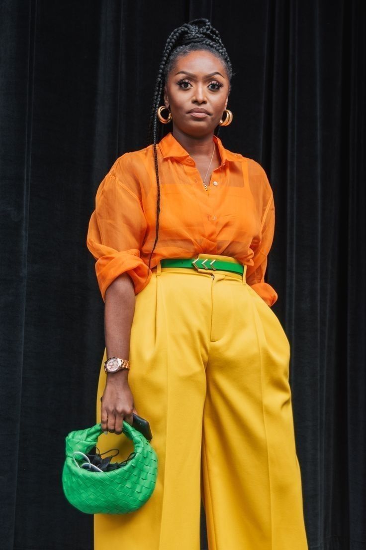 Mulher usando um look vibrante da paleta de primavera com blusa laranja, calça amarela e acessórios verdes, destacando seu estilo alegre e colorido.