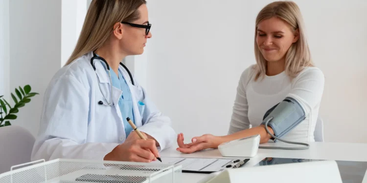 Mulher realizando exame de pressão arterial com a supervisão de uma médica. Importante para o check-up anual de saúde.
