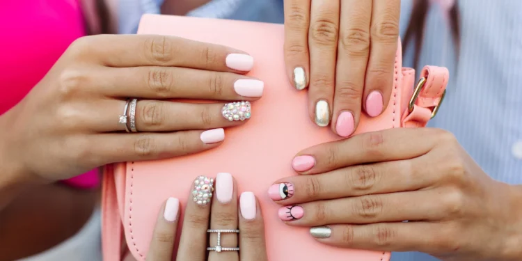 Unhas bem cuidadas e decoradas, com designs e detalhes variados, sobre um fundo claro.