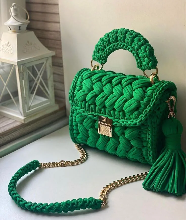 Bolsa de crochê verde com alça de corrente dourada e detalhe em tassel, combinando estilo e sofisticação.