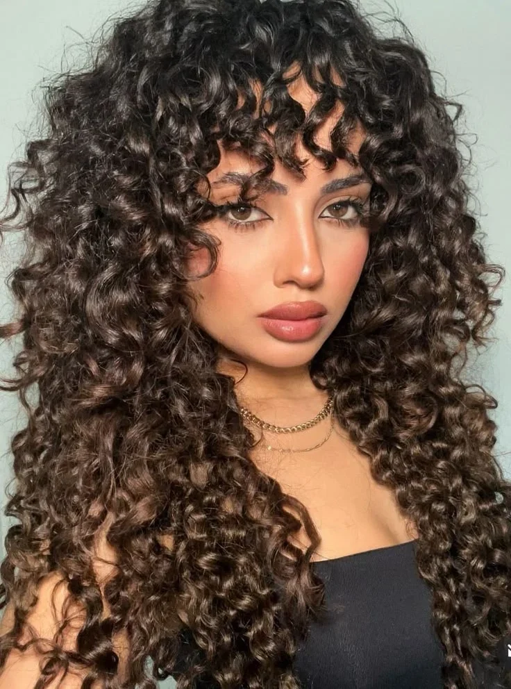 Mulher com cabelo cacheado longo em camadas e franjas modernas