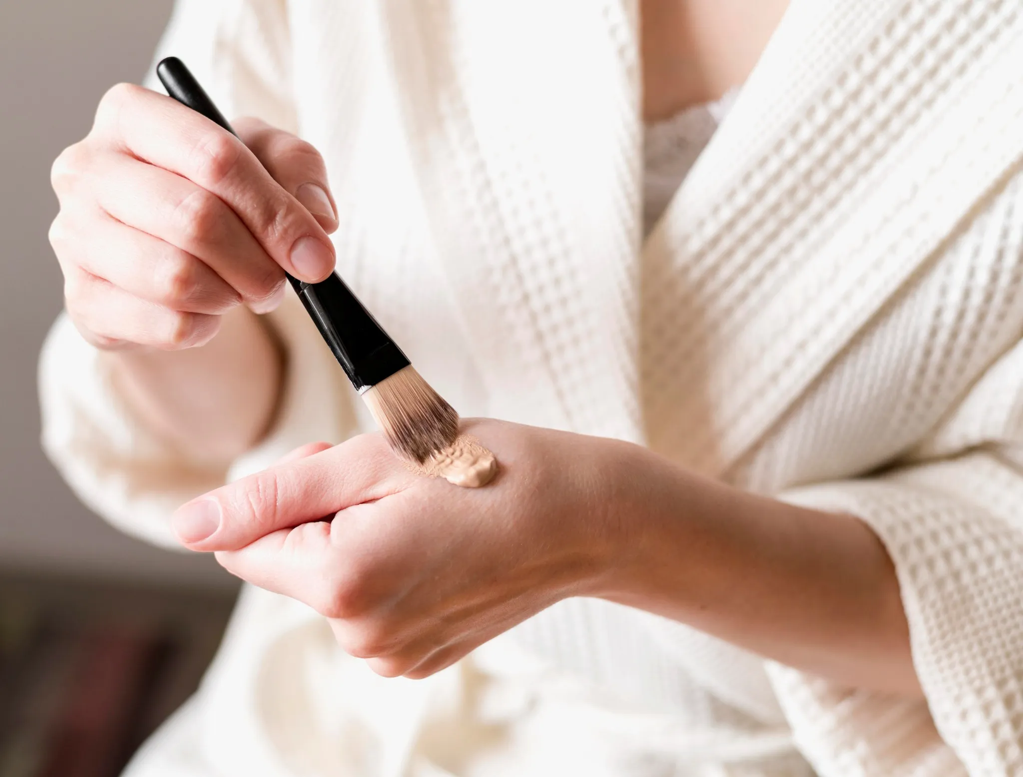 Mulher aplicando base com pincel em sua mão, transmitindo leveza e naturalidade na maquiagem.