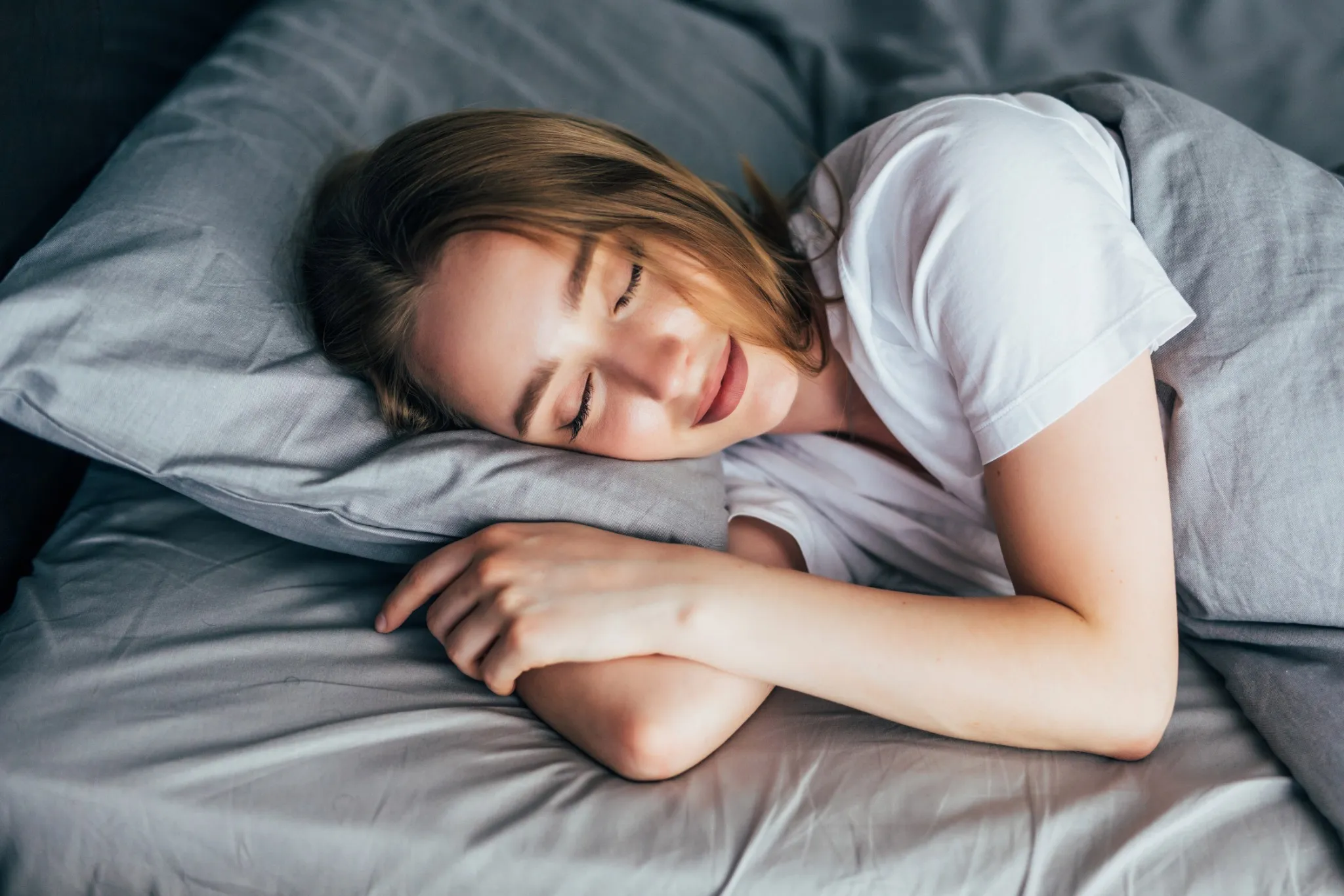 Mulher dormindo tranquilamente, descansando em uma cama com lençóis cinza