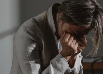 Mulher sobrecarregada emocionalmente, com as mãos cobrindo o rosto, refletindo o estresse e a pressão de múltiplas responsabilidades.