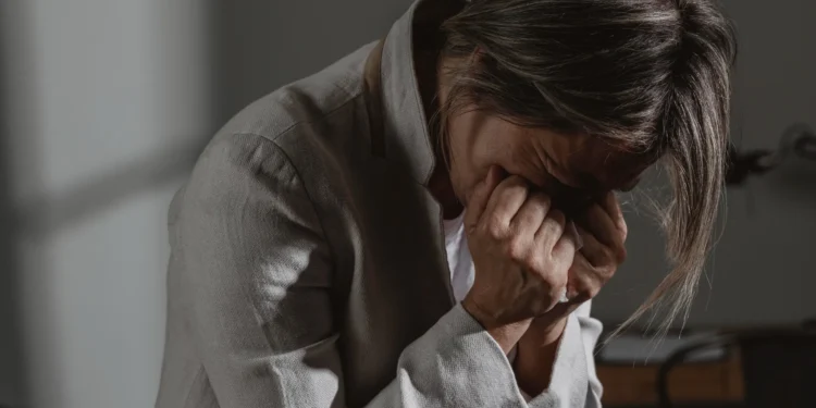 Mulher sobrecarregada emocionalmente, com as mãos cobrindo o rosto, refletindo o estresse e a pressão de múltiplas responsabilidades.