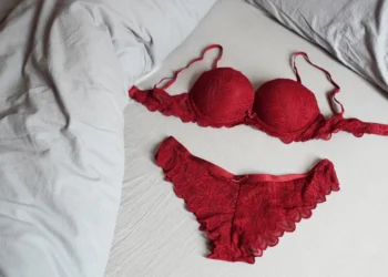 Conjunto de lingerie vermelha sobre uma cama com lençóis brancos, mostrando o sutiã e a calcinha de renda delicada.